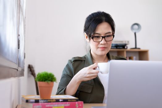 Modern young Asian woman working from home and drinking a coffee.