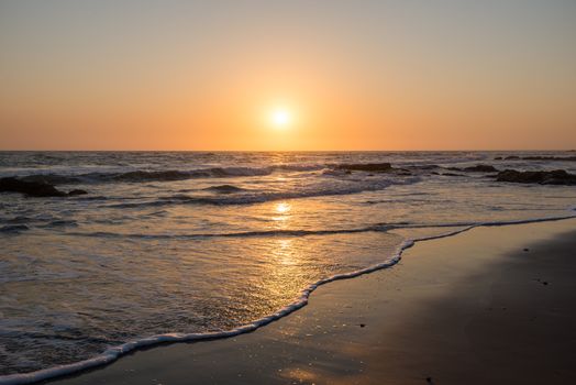 A colorful sunset with low sun and small waves at Atlantic Ocean Coast near Namibian Desert