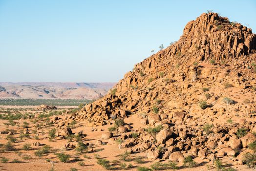 Rocky landscape of Kunene Region at Namibian winter with huge boulders and green trees