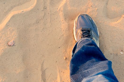 Top down view of man extending a foot with a worn sneaker jeans on dusty sand showing travel and trekking during evening as sunlight bounces off it. Shows wanderlust and travel in India which has been stopped by the lockdown and the epidemic