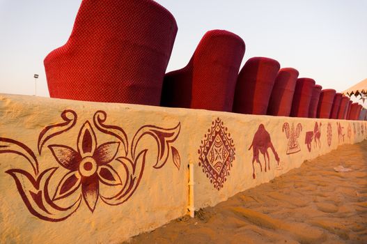 Close up shot of red muddha cane chairs sofas with small yellow brick walls for seating visitors during a performance with desert sand in the background. Shot in the evening it shows the hours just before the traditional dances and performances start