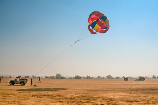 Jeep towing a parachute for adventure para gliding in the empty barren thar desert in rajasthan near jaisalmer and sum. Shows the various adventure sport options available on road trips in this state