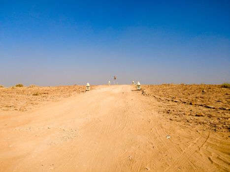 Empty dirt road with barren desert on both sides and blue sky above showing thar desert of rajasthan india.