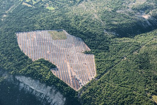 Mid-air view of solar panels of a new solar power plant, surrounded by green forest of Provence