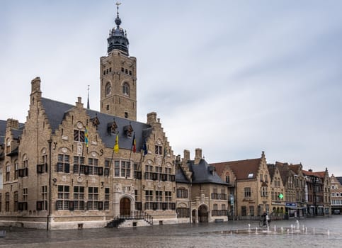 Diksmuide, Flanders, Belgium -  June 19, 2019: Grote Markt. Wider shot of Brown brick historic City Hall, or Stadhuis, building under light blue sky. Rain Wet market square. Pharmacy light, bike rider.