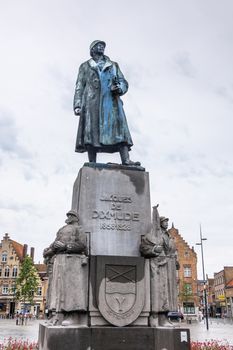 Diksmuide, Flanders, Belgium -  June 19, 2019: Grote Markt. Bronze statue of General Jacques de Dixmude on gray stone pedestal against silver sky. Some Yellowish brown house facades.