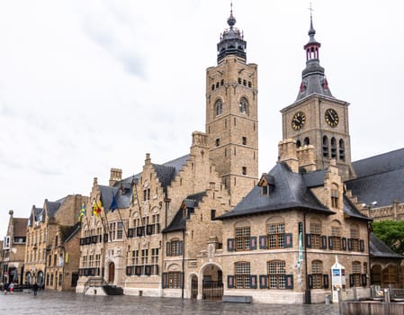 Diksmuide, Flanders, Belgium -  June 19, 2019: Grote Markt. Brown brick historic City Hall, or Stadhuis, building under gray sky. Rain Wet market square. Saint Nicolas church clock tower in back.