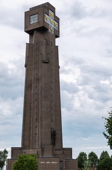 Diksmuide, Flanders, Belgium -  June 19, 2019: Closeup of IJzertoren, tallest peace monument of WW 1 against gray blue cloudscape. Dutch words saying No More War. Some green foliage.