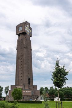 Diksmuide, Flanders, Belgium -  June 19, 2019: IJzertoren, tallest peace monument of WW 1 against gray blue cloudscape. Dutch words saying No More War. Some green foliage and lawn.