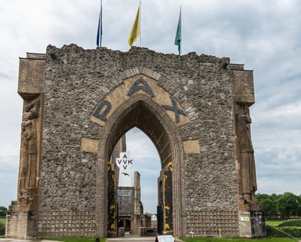 Diksmuide, Flanders, Belgium -  June 19, 2019: Black on White Crypt memorial, remnants of dynamited tower, and Pax gate in front with sculptures under gray sky and some green foliage.