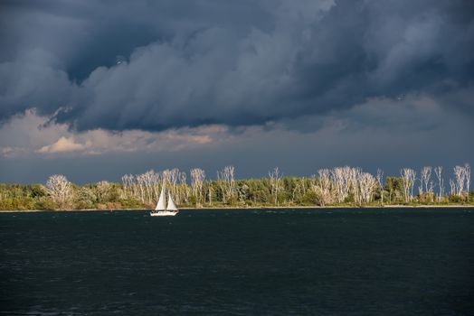 Lonely white sailing boat between dark water and depressing clouds, Toronto, Canada