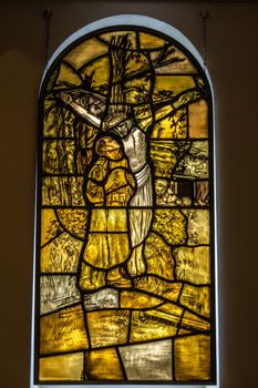 Diksmuide, Flanders, Belgium -  June 19, 2019: Yellowish Stained glass window in chapel of IJzertoren, depicting soldier with helmet in hand standing under Jesus cross.