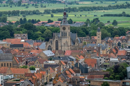 Diksmuide, Flanders, Belgium -  June 19, 2019: View on dowtown from up IJzertoren, tallest peace monument of WW 1. Brick buildings with red roofs, towers of church and city hall, green pasture.