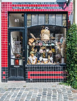 Gent, Flanders, Belgium -  June 21, 2019: Red and black facade with display window of Louise and Madeleine vintage store on Kraanlei. Some green foliage and gift items on display.