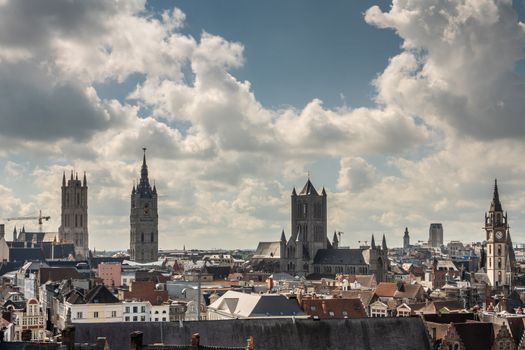 Gent, Flanders, Belgium -  June 21, 2019: Shot from castle tower, view over city roofs shows six most important and historic towers of Belfry, churches, Postal service, and university, under white cloudscape with blue patches.