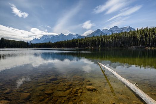 The sun is rising above the Herbert Lake and lighting up underwater stones and distant Rocky Mountains of Alberta, Canada