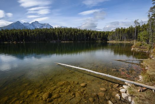 The sun is rising above the Herbert Lake and lighting up underwater stones and distant Rocky Mountains of Alberta, Canada