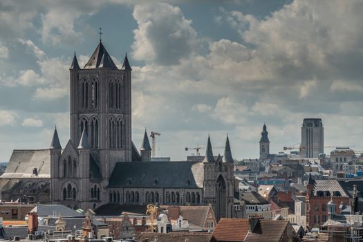 Gent, Flanders, Belgium -  June 21, 2019: Shot from castle tower, view over city roofs shows Sint Niklaas church with in back towers of University and Onze-Lieve-Vrouw-Sint-Pieters church under heavy cloudscape.