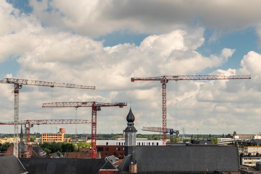 Gent, Flanders, Belgium -  June 21, 2019: Shot from castle tower, view over city roofs shows closeup of tower and roof of Saint Augustine cloiser and tower with plenty of cranes in back under heavy cloudscape.