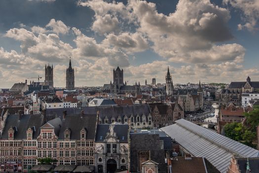Gent, Flanders, Belgium -  June 21, 2019: Shot from castle tower, view over city roofs shows six most important and historic towers of Belfry, churches, Postal service, and university. Fish market gate. Cloudscape with blue patches.