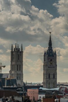 Gent, Flanders, Belgium -  June 21, 2019: Shot from castle tower, view over city roofs shows towers of Belfry and Cathedral. Cloudscape with blue patches.