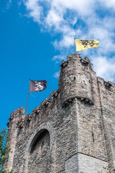 Gent, Flanders, Belgium -  June 21, 2019: Corner of Gray stone tower of Gravensteen, historic medieval castle of city against blue sky with white clouds. Flags on top,