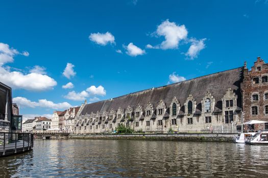 Gent, Flanders, Belgium -  June 21, 2019: Historic gray-stone long facade of Vleeshuis, medieval meat trading floor, along Leie River under blue sky with white clouds..