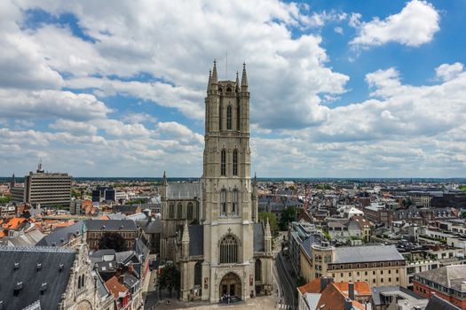 Gent, Flanders, Belgium -  June 21, 2019: Shot from top Belfry. Sint-Baafs Cathedral and closeup of tower against blue sky with cloudscape. Cityscape of roofs and buildings up to flat horizon.