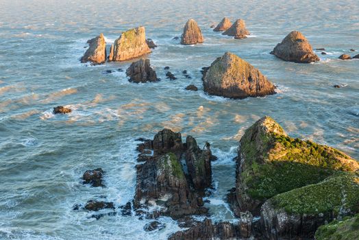 The setting sun illuminates boulders and waves of Nugget Point, the end of the New Zealand