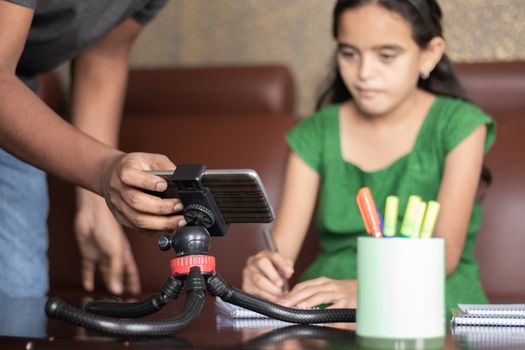 Father helping daughter by adjusting mobile to studying the lesson of online class or e-learning - concept of Role of parent in supporting child during virtual class, homeschooling, distance learning