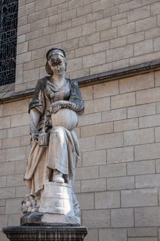 Brussels, Belgium - June 22, 2019: Closeup of Beige stone statue with black mold of the Milkmaid, serving milk out of jug against beige stone wall of Saint Nicolas Church.