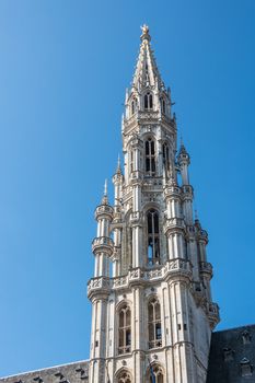 Brussels, Belgium - June 22, 2019: Closeup of gray stone spire of city hall on Grand Place against blue sky. Golden Saint Michael statue on top.