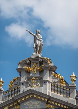 Brussels, Belgium - June 22, 2019: Statue of Saint Homobonus of Cremona on top of gable of La Chaloupe D’Or buidling on Grand Place against blue sky with white clouds. Golden decorations on gray stone.