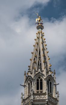 Brussels, Belgium - June 22, 2019: Closeup of gray stone spire of city hall on Grand Place against blue sky with white clouds. Golden Saint Michael statue on top.