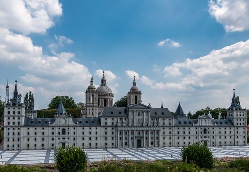 Brussels, Belgium - June 22, 2019: Mini-Europe exhibition park. Royal site of San Lorenzo de el Escorial built in miniature under blue sky with white cloudscape. Green foliage in front.