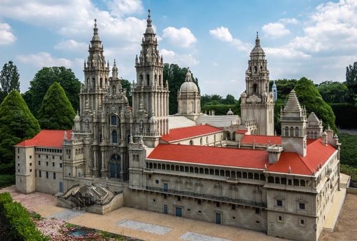 Brussels, Belgium - June 22, 2019: Mini-Europe exhibition park. Santiago de Compostela Cathedral in miniature set in green foliage environment against blue sky with white cloudscape. Brown stone and red roofs.