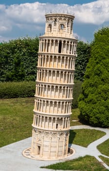 Brussels, Belgium - June 22, 2019: Mini-Europe exhibition park. Closeup of Leaning Tower of Pisa in miniature against green foliage under blue sky with white cloudscape.