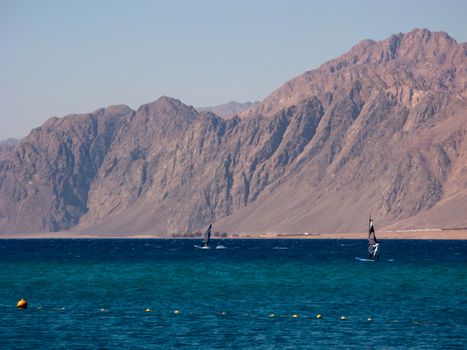 Windsurfers are in the Dahab's gulf with the distant mountain background