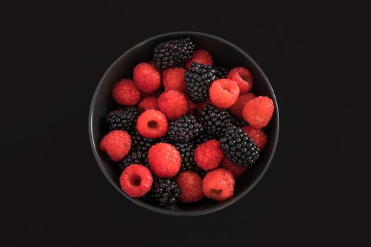 Blackberries and raspberries in a black bowl. Black background. Top view.