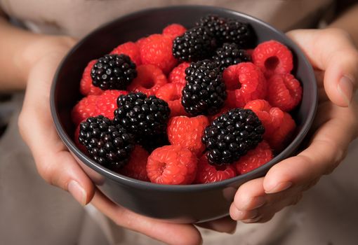 Female hands holding a bowl full of blackberries and raspberries.
