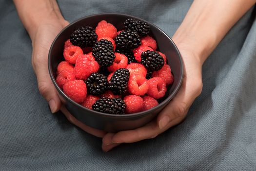 Female hands holding a bowl full of blackberries and raspberries.