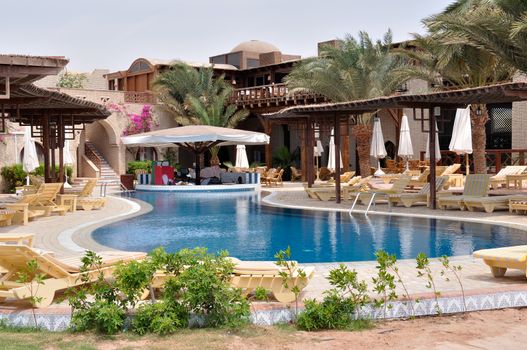 Relaxing picture of the cold hotel swimming pool with clear water and some chairs, trees and lounges around