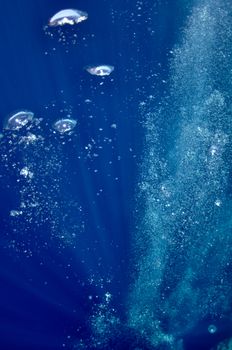 The picture shows underwater bubbles which raise from the depth of blue sea