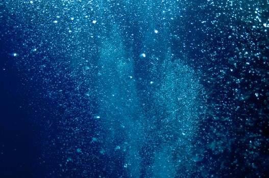 The picture shows underwater bubbles which raise from the depth of blue sea