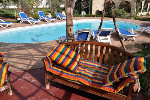 Relaxing picture of the cold hotel swimming pool with clear water and some chairs, trees and lounges around