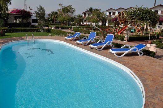 Relaxing picture of the cold hotel swimming pool with clear water and some chairs, trees and lounges around