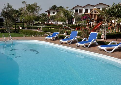 Relaxing picture of the cold hotel swimming pool with clear water and some chairs, trees and lounges around