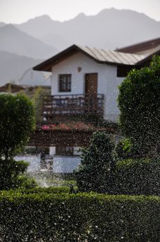 A lot of water drops on a poured green lawn and misty houses and mountains on the background