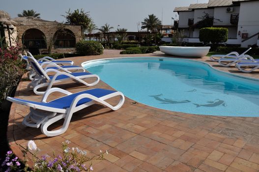 Relaxing picture of the cold hotel swimming pool with clear water and some chairs, trees and lounges around