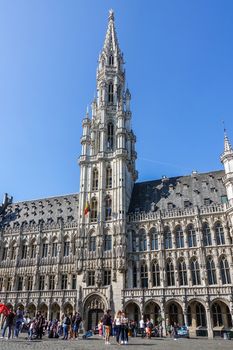 Brussels, Belgium - June 22, 2019: Grand Place with tourists and gray stone City hall building with spire amd Be;gian flag against blue sky.